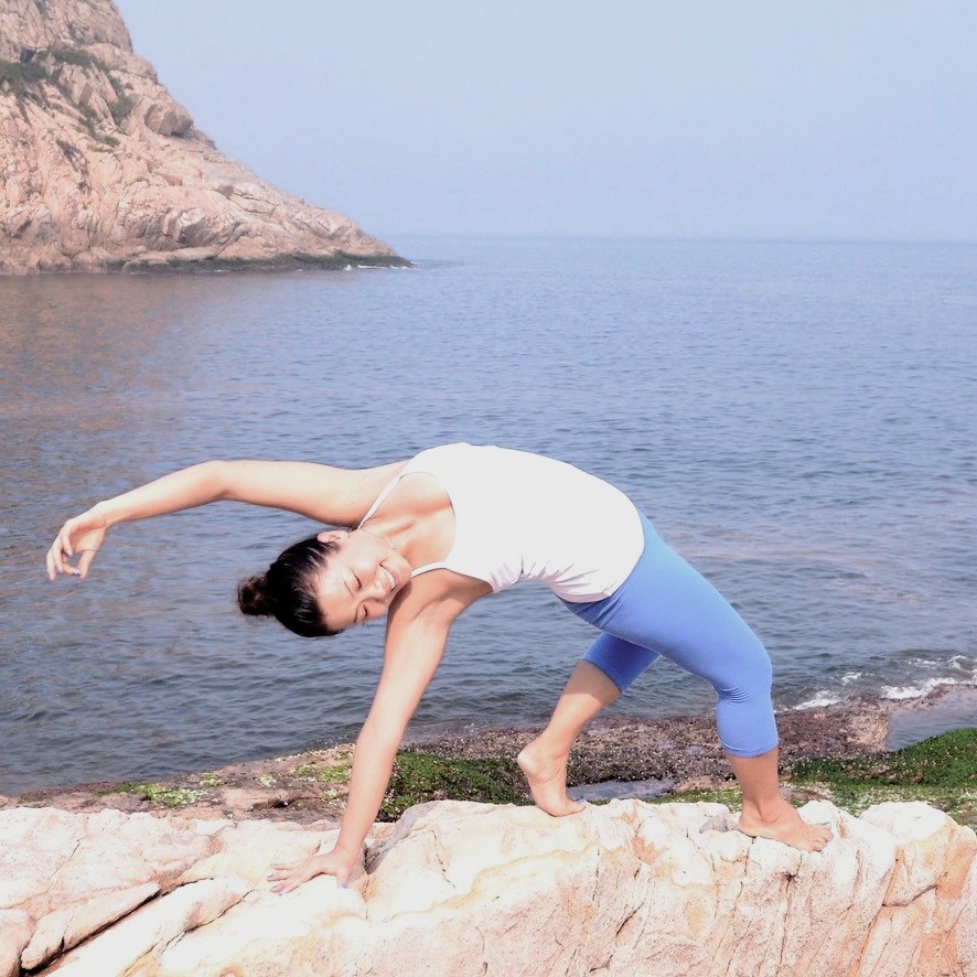 Rachel in a joyful side-stretch pose on coastal rocks