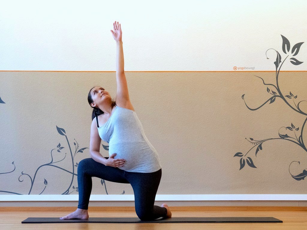 A pregnant student in a kneeling lunge pose with arm raised