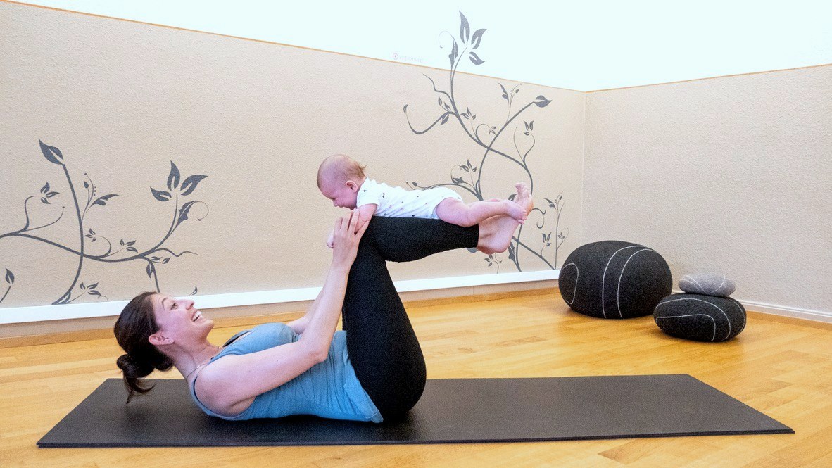 A new mother practicing yoga with her baby balanced on her shins