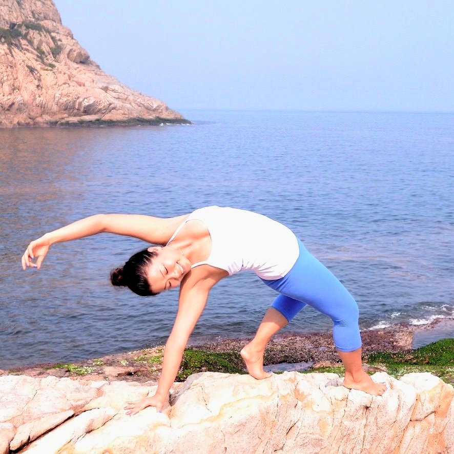 Rachel in a joyful side-stretch pose on coastal rocks