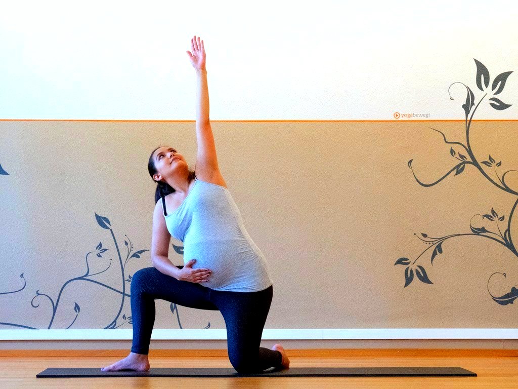 A pregnant student in a kneeling lunge pose with arm raised